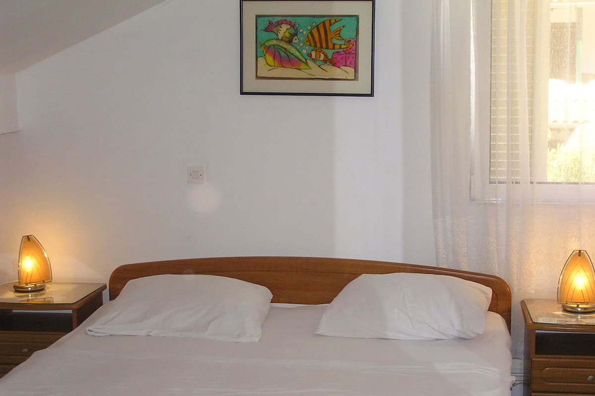Un dormitorio con cabecera de madera, dos lámparas de noche, un cuadro enmarcado en la pared y una ventana con persianas.
