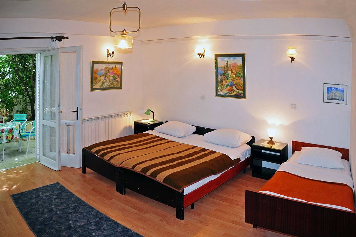 Un dormitorio con dos camas, piso de madera y puerta de cristal que da a un espacio exterior.