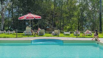 Relax by the serene pool surrounded by lush greenery and lounge under the shade of an umbrella.
