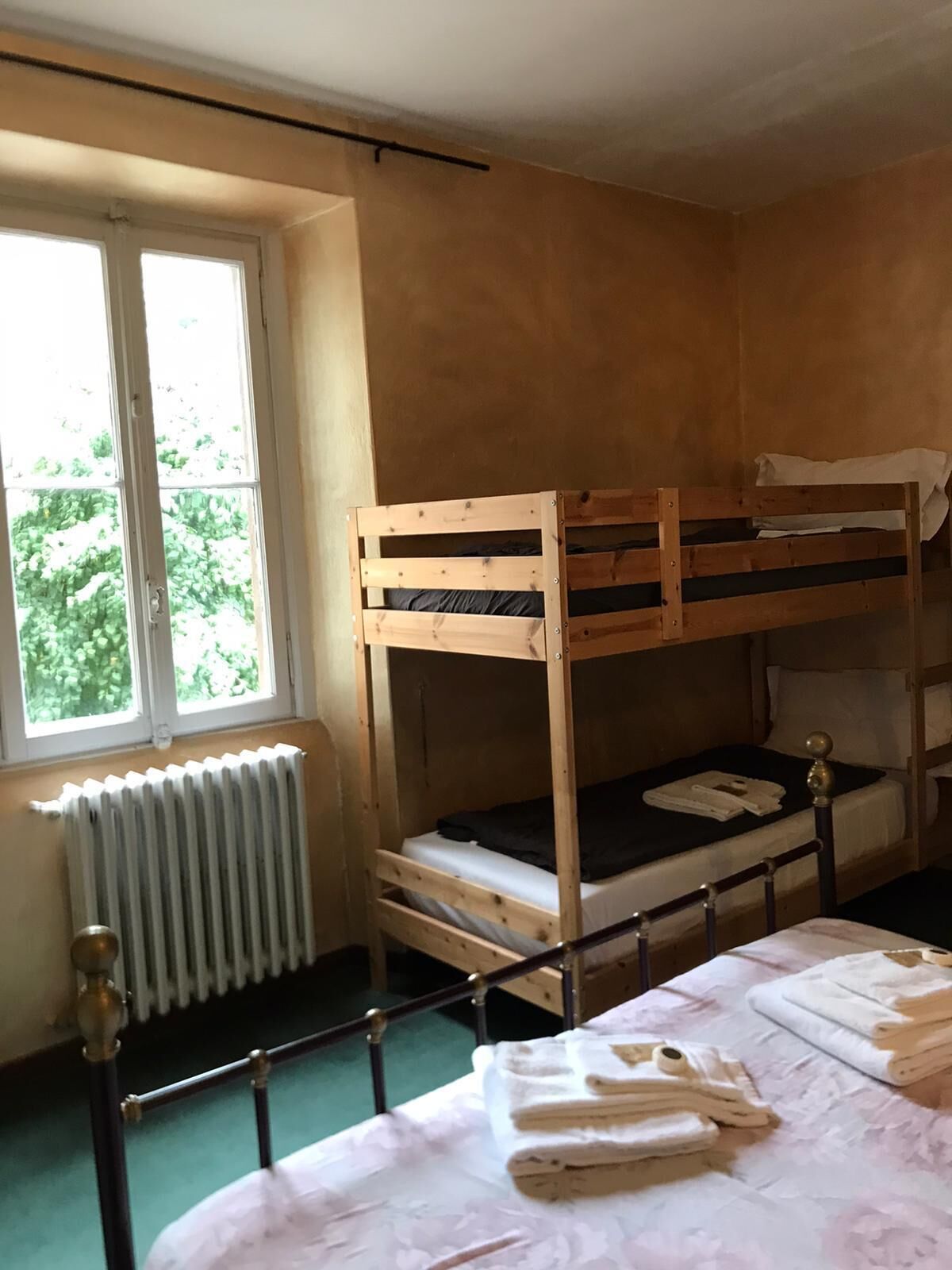 A bunk bed room with a window, radiator, and neatly folded towels on the bed.