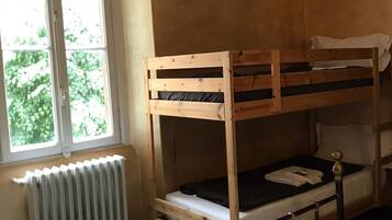 A bunk bed room with a window, radiator, and neatly folded towels on the bed.