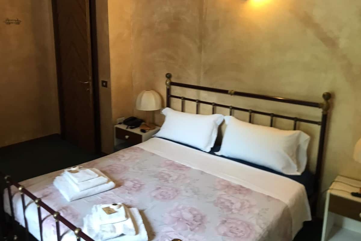 A hotel room with a bed, a nightstand with a lamp, and a door.