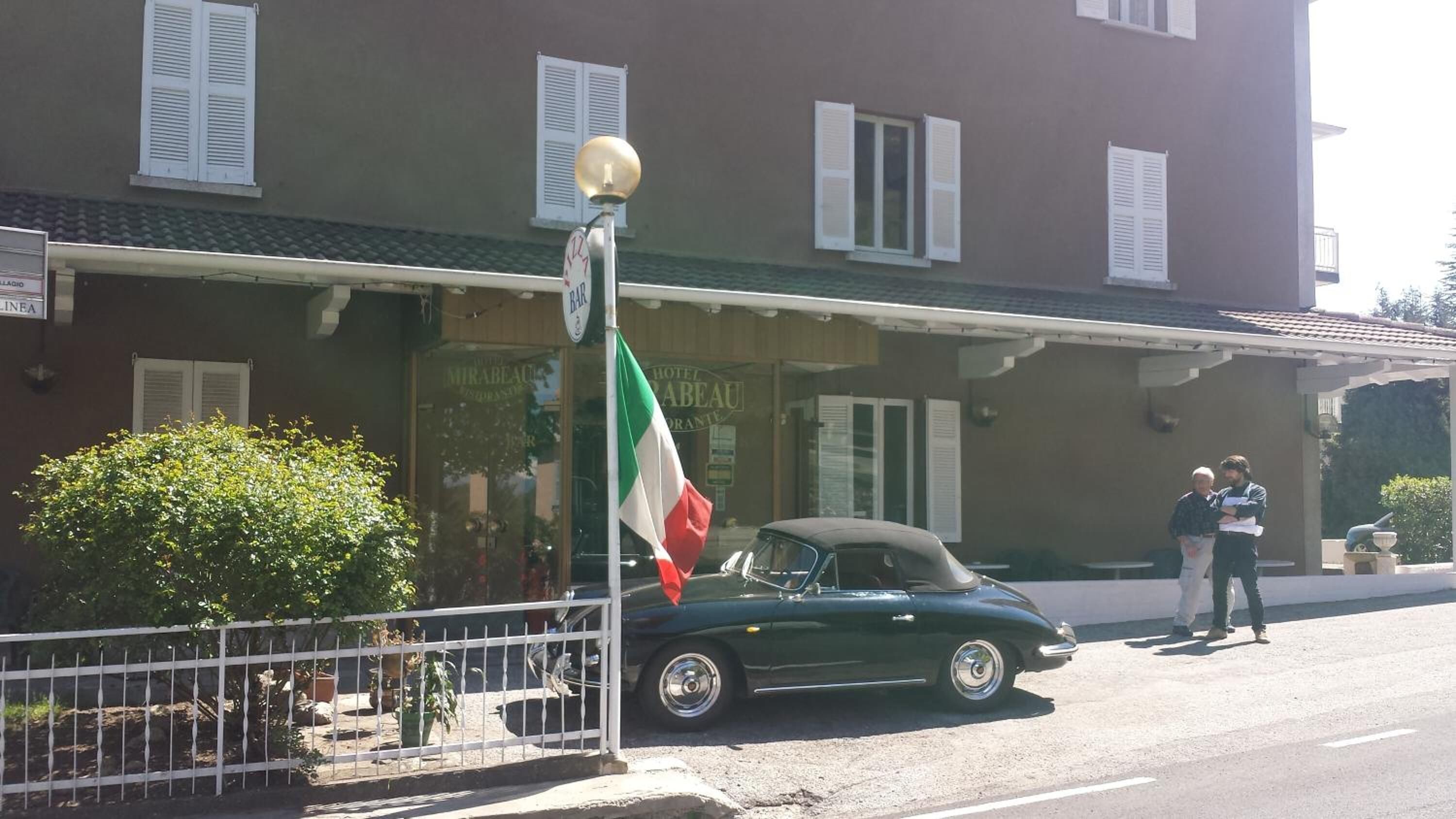 Un coche verde antiguo estacionado frente a un edificio con un cartel que dice "Hotel Mirabeau".