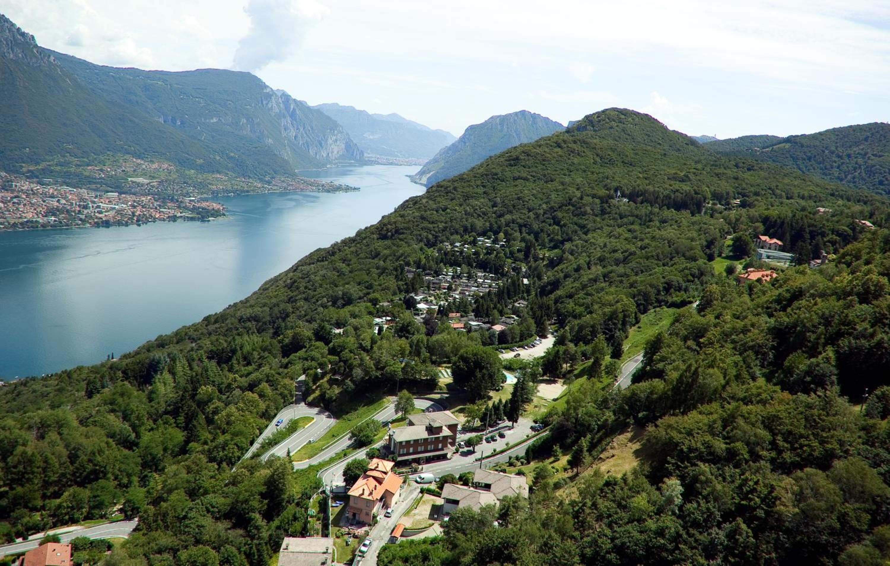 An aerial view of a lakeside town with a mix of residential and commercial buildings, surrounded by lush greenery and mountains.