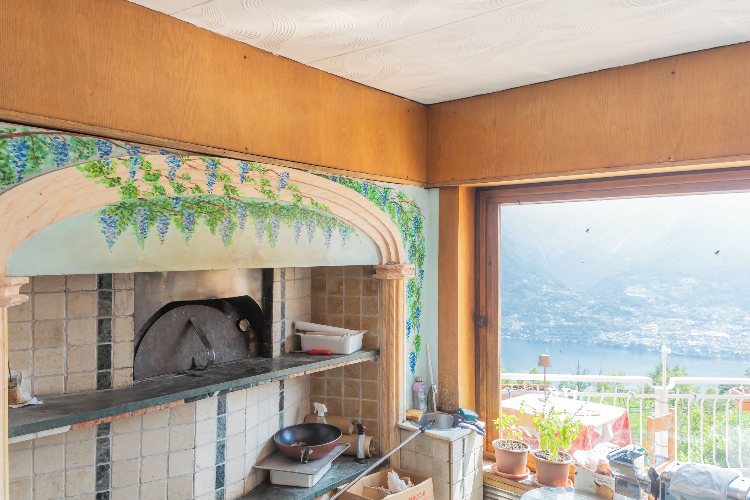 A kitchen with a view of a lake and mountains, featuring a tiled backsplash, wooden cabinets, and a variety of kitchen utensils and appliances.