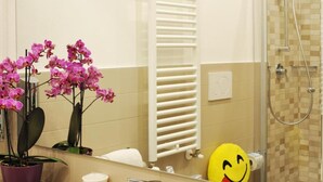 A bathroom with a shower, a sink, a mirror, a towel rack, and a potted orchid plant.