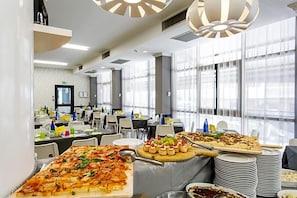 A buffet setup with a variety of food items, including a large pizza, appetizers, and stacked plates.