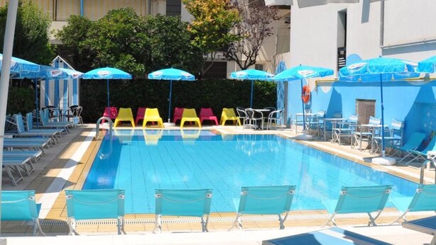 A swimming pool with blue and white striped umbrellas, yellow and pink lounge chairs, and a tiled deck area.