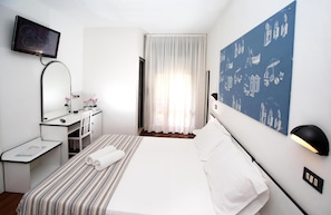 A hotel room with a bed, a desk, a chair, a television, and a wall with a nautical-themed mural.