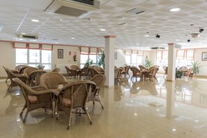 Un hall d’entrée spacieux, doté de meubles en osier, de grandes fenêtres et d’un sol carrelé.