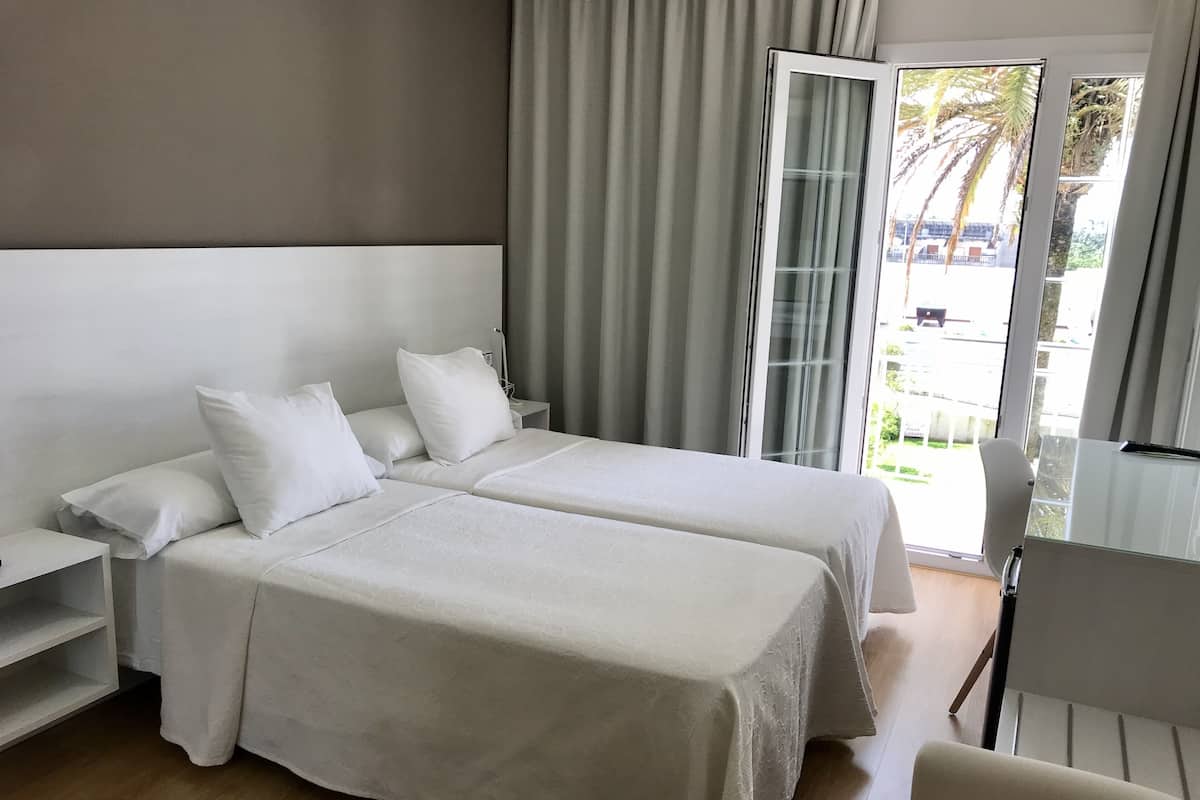 Een hotelkamer met twee bedden, een bureau, een stoel en een schuifdeur naar een balkon.