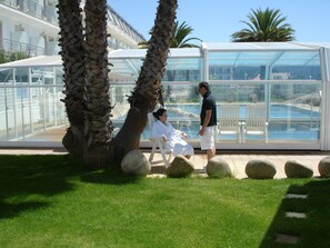 Un espace aménagé au bord de la piscine, doté d’une structure en verre, de palmiers et d’un coin salon.