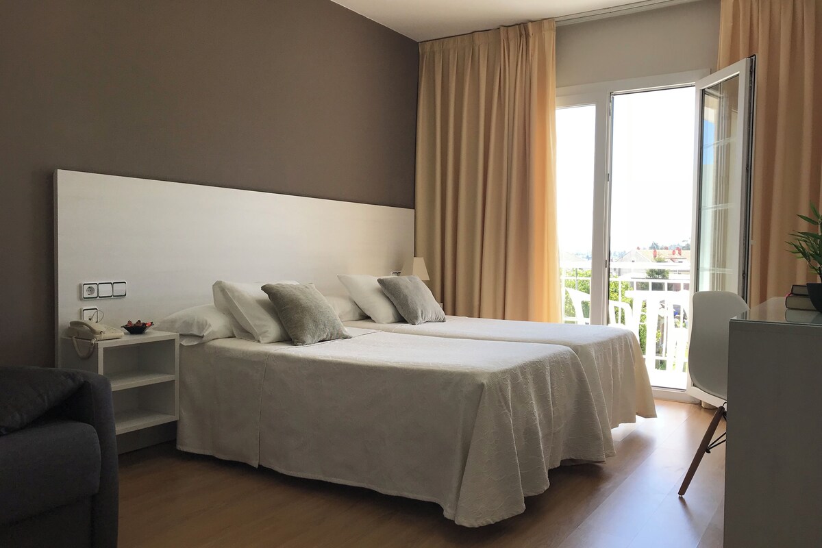 Habitación de hotel con una cama grande, mesitas de noche, un escritorio y vistas a la ciudad desde la ventana.