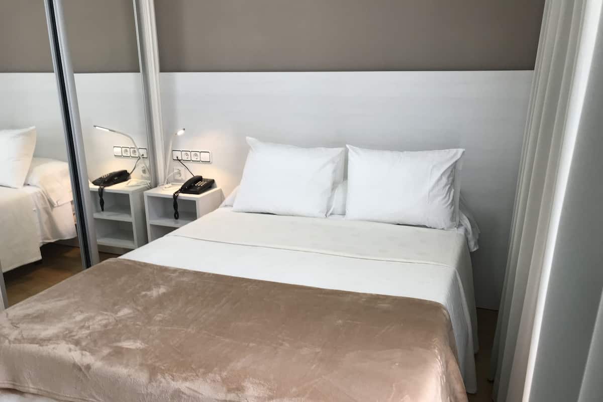 Een hotelkamer met een bed, witte beddengoed, een nachtkastje met een lamp en een telefoon.