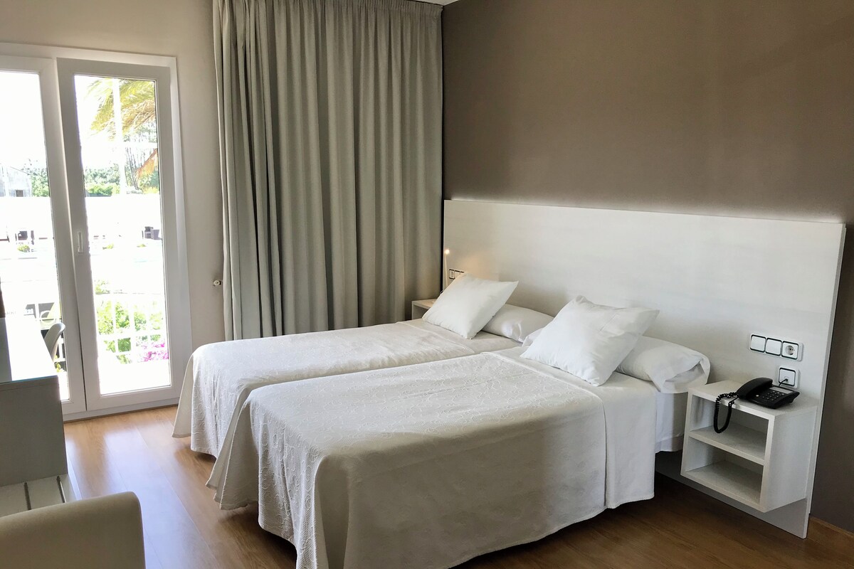 Habitación de hotel con dos camas, un escritorio, una silla y un teléfono sobre una mesita de noche.
