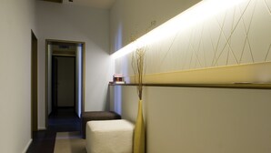 A hallway with a white wall, a marble floor, a bench, and a tall vase with branches. - Romeo al Babuino (Rome)