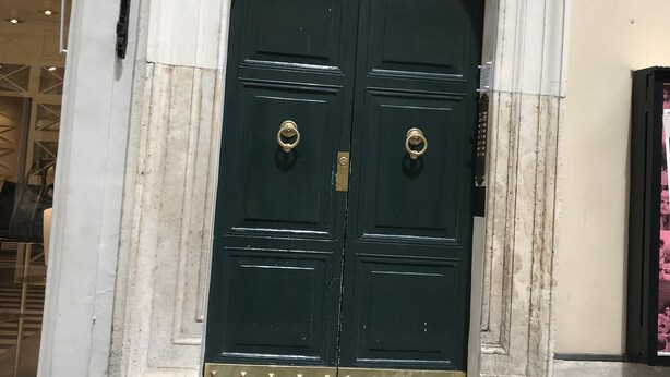 A dark green double door with brass handles, set within a white stone frame, and a small step leading up to it. - Romeo al Babuino (Rome)