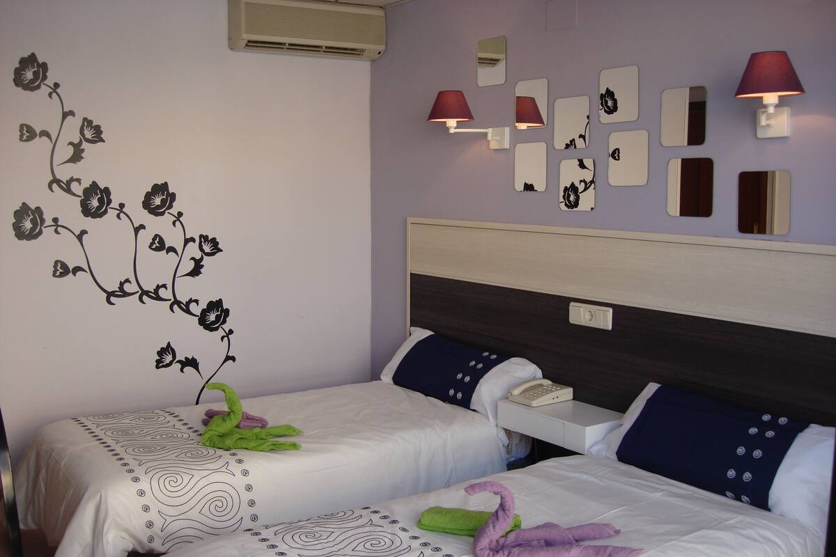 A hotel room with two beds, each with a unique floral bedspread, a bedside telephone, and wall-mounted mirrors.