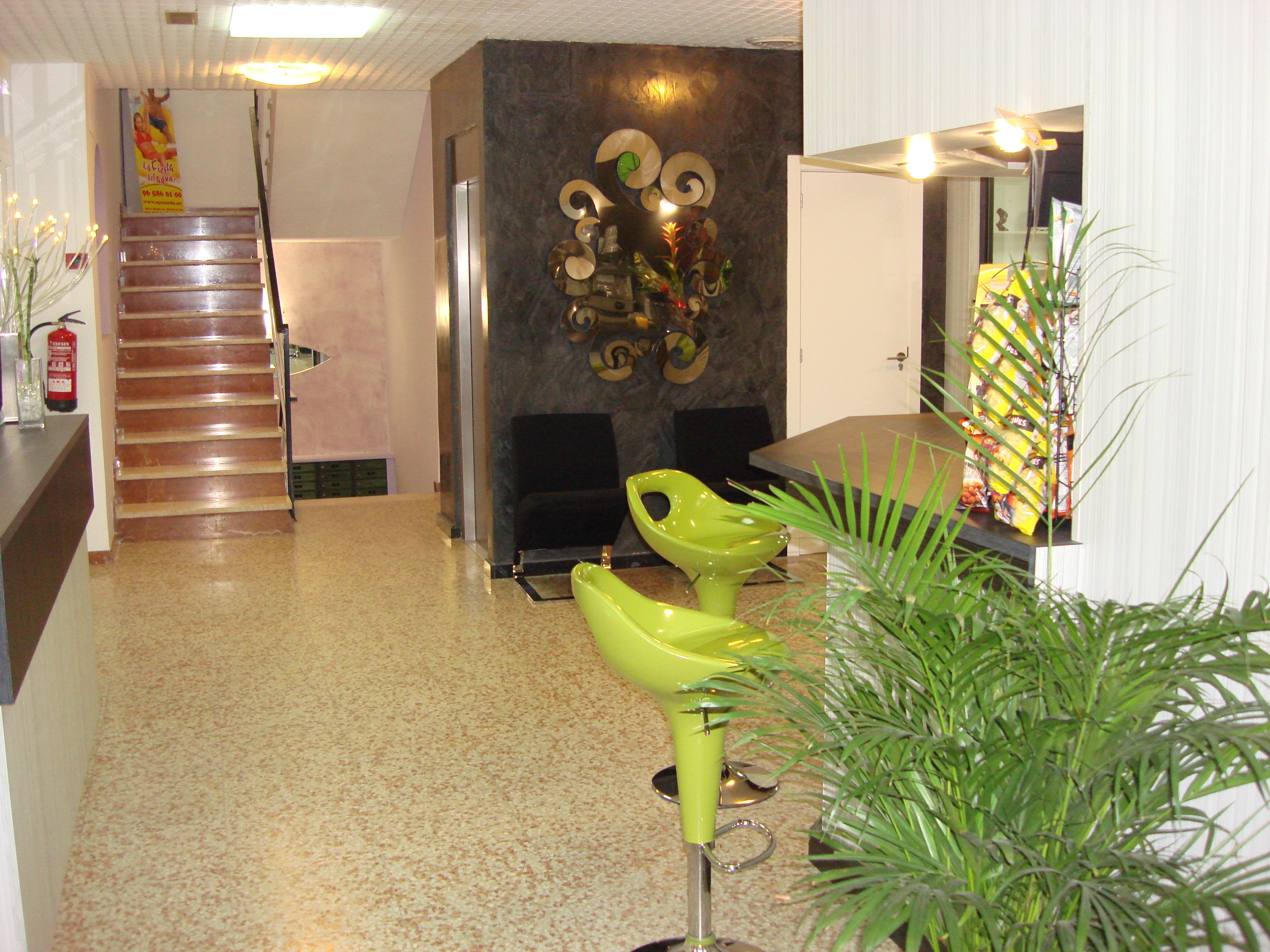 Un vestíbulo de hotel con una escalera, un mostrador de recepción y una zona de estar con sillas verdes.