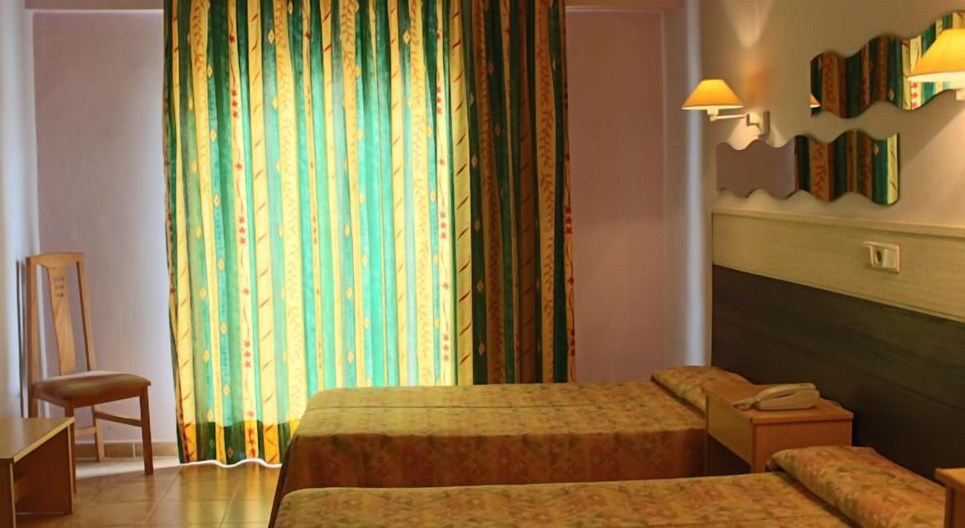 A hotel room with two beds, a chair, a desk, and a telephone.