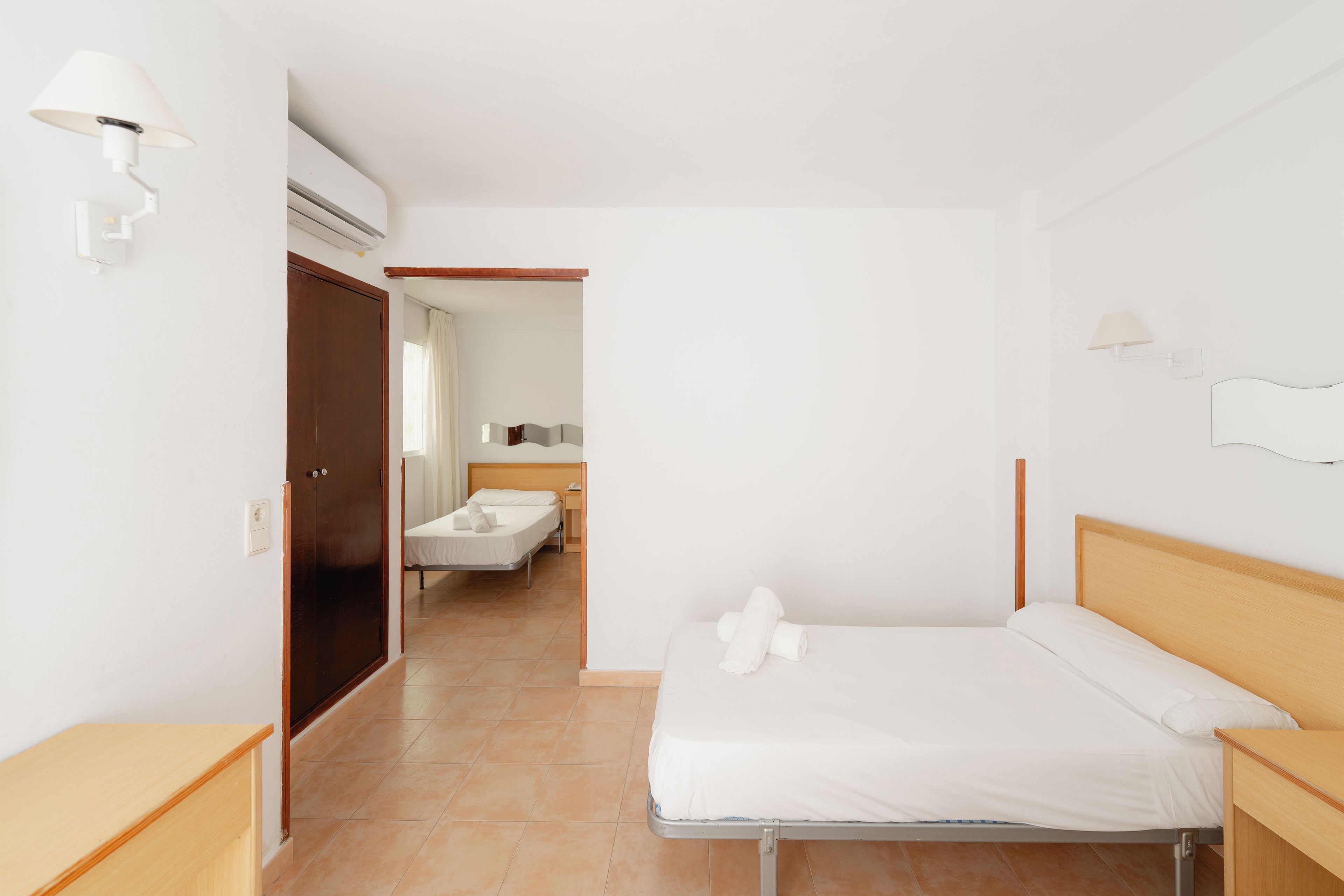 Habitación de hotel con una cama individual, una mesita de noche de madera, una lámpara de pared y un equipo de aire acondicionado.