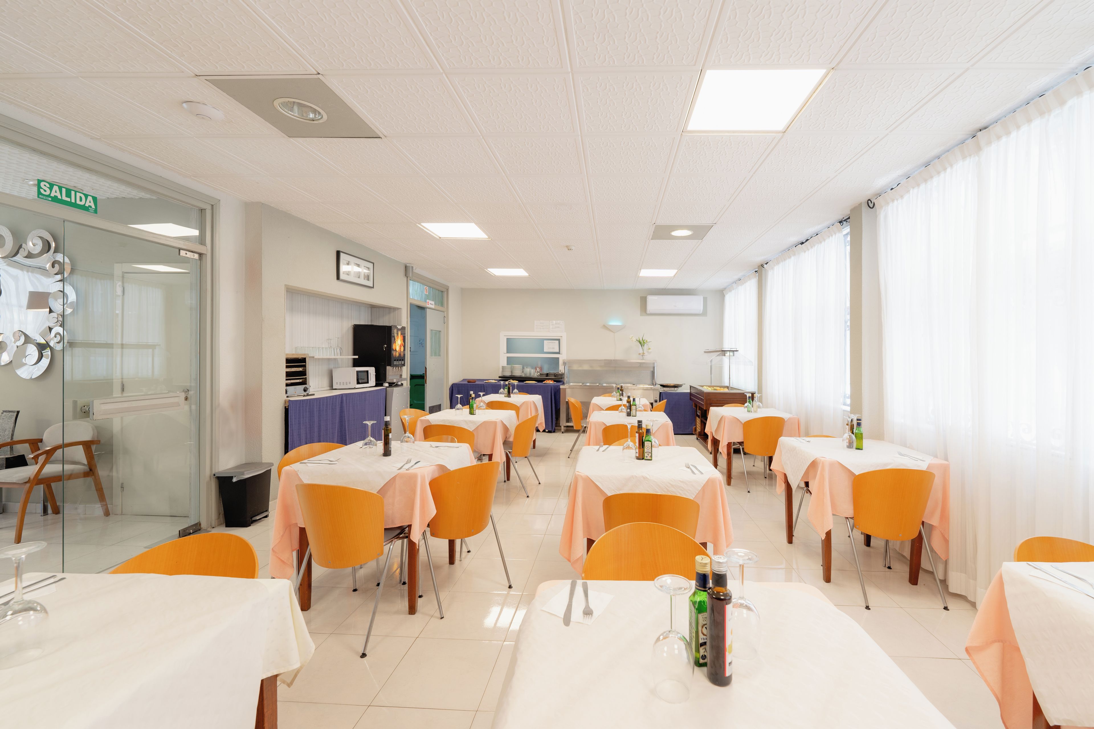 A dining area with tables set for meals, chairs, and a kitchen area in the background.