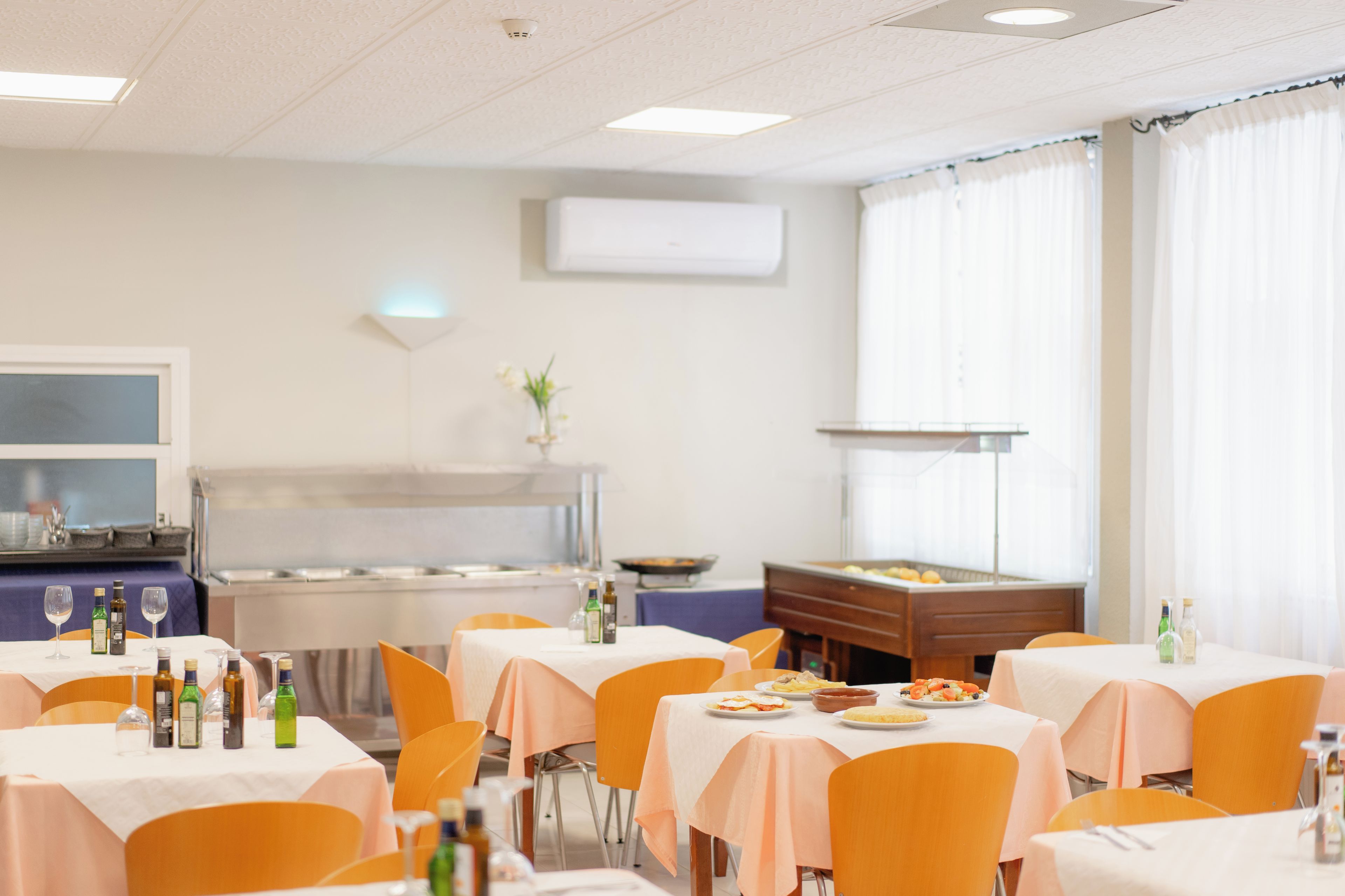 Ein Essbereich mit gedeckten Tischen, einer Speiseauswahl vom Buffet und einer Küche im Hintergrund.