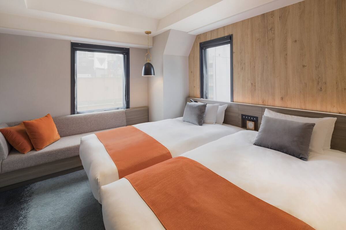Una habitación de hotel con dos camas, un sofá y una ventana.