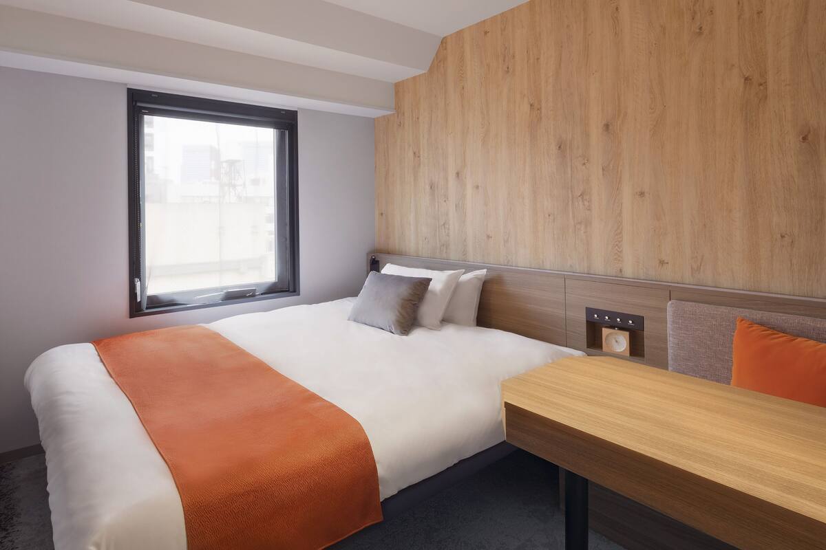 Una habitación de hotel moderna con una cama grande, un cabecero de madera, una mesita de noche y una ventana con vistas.