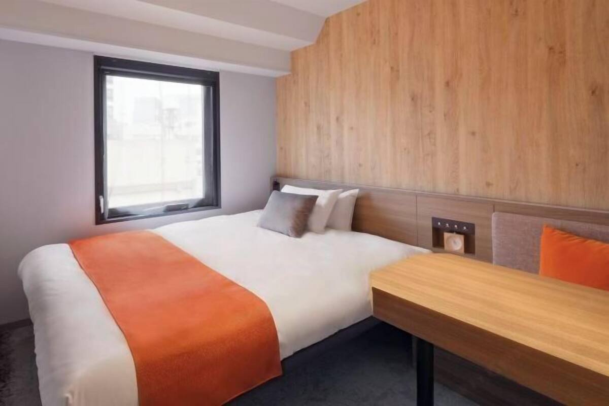 Habitación de hotel con cama, cabecera de madera, ventana y una mesa.