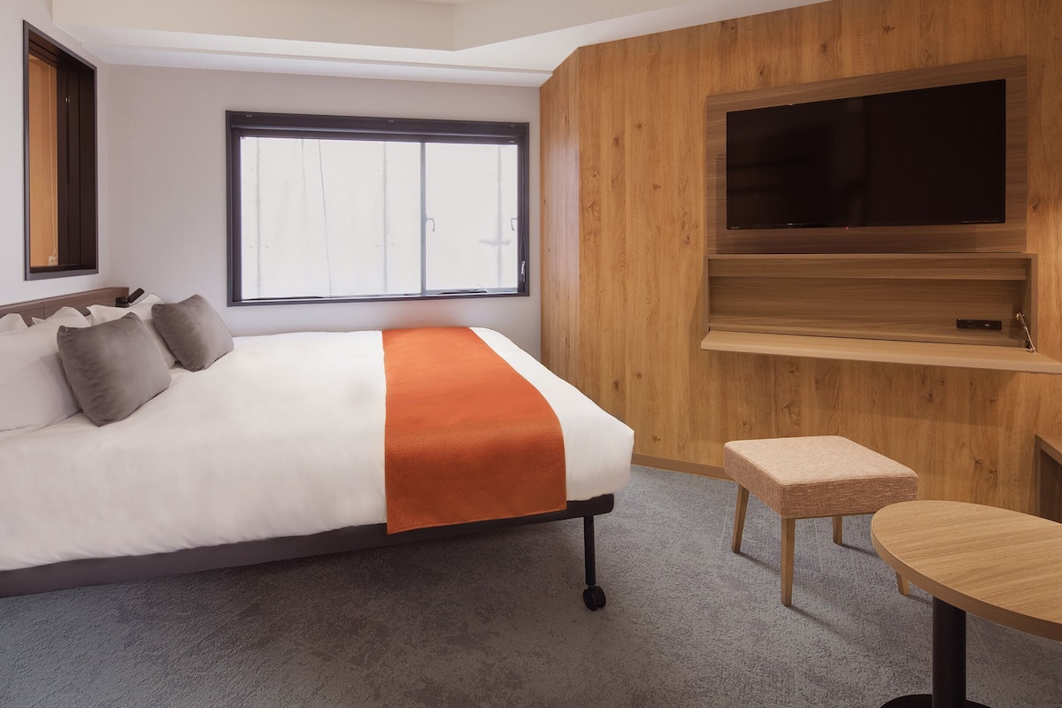 Una habitación de hotel moderna con cama, televisor, una mesita y ventana.
