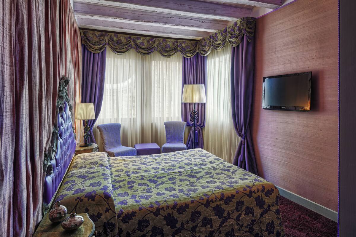 A hotel room with a large bed, two chairs, a TV, and a lamp.
