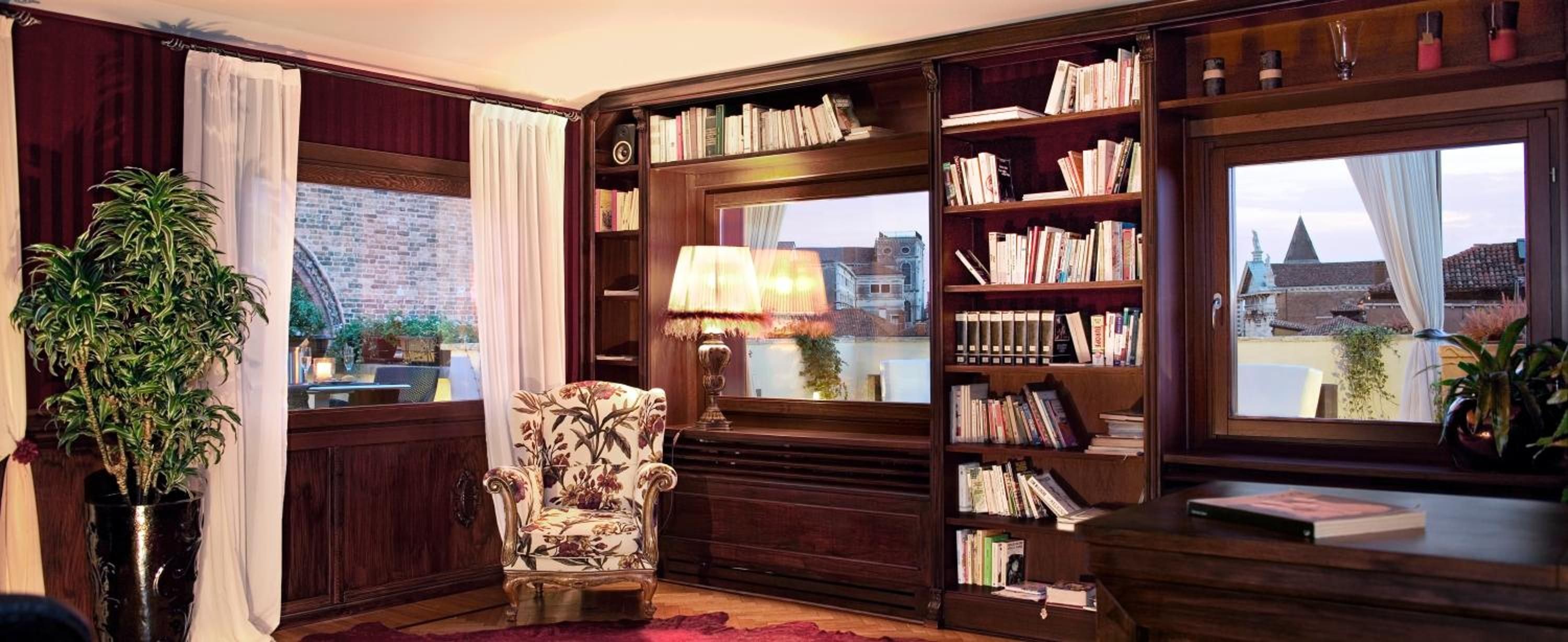 A cozy reading nook with a large bookshelf, a comfortable armchair, and a view of a cityscape through a window.