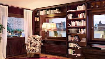 A cozy reading nook with a large bookshelf, a comfortable armchair, and a view of a cityscape through a window.