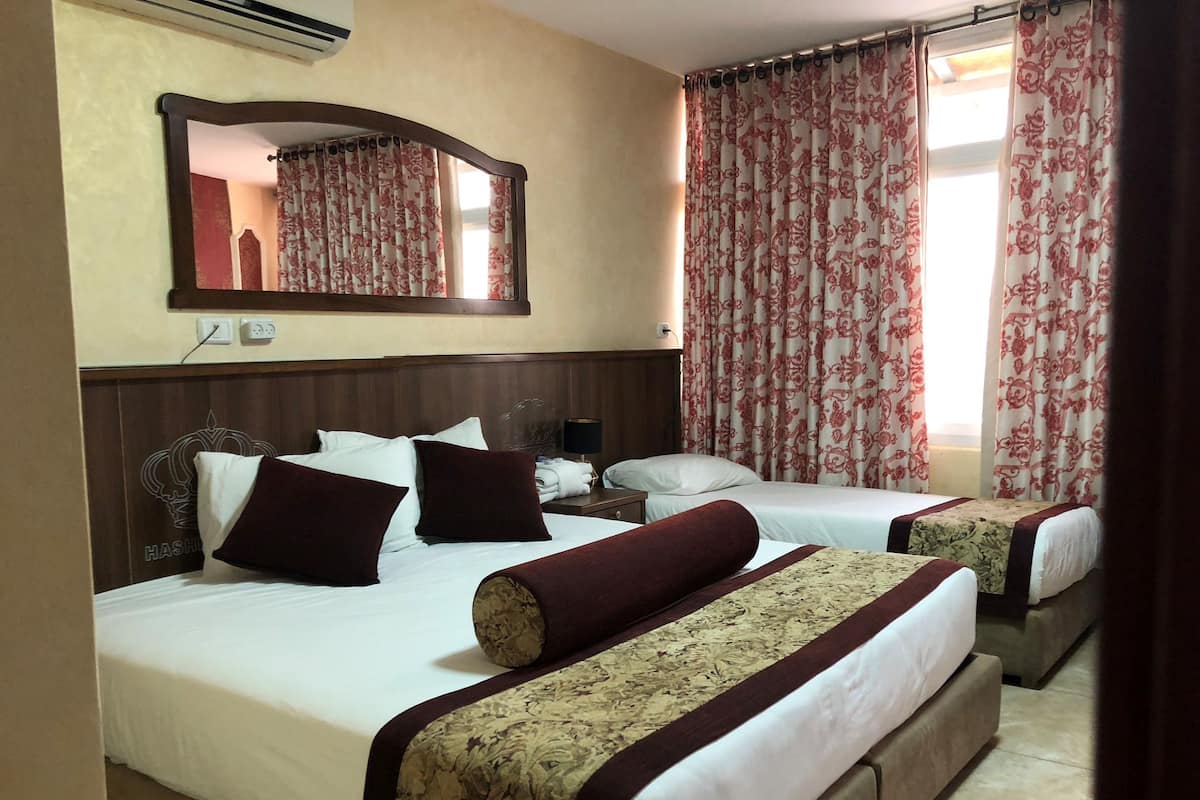 A hotel room with two beds, a large mirror, and floral curtains.