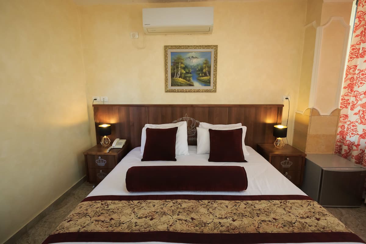 A hotel room with a large bed, two bedside tables with lamps, a painting on the wall, and a red curtain.