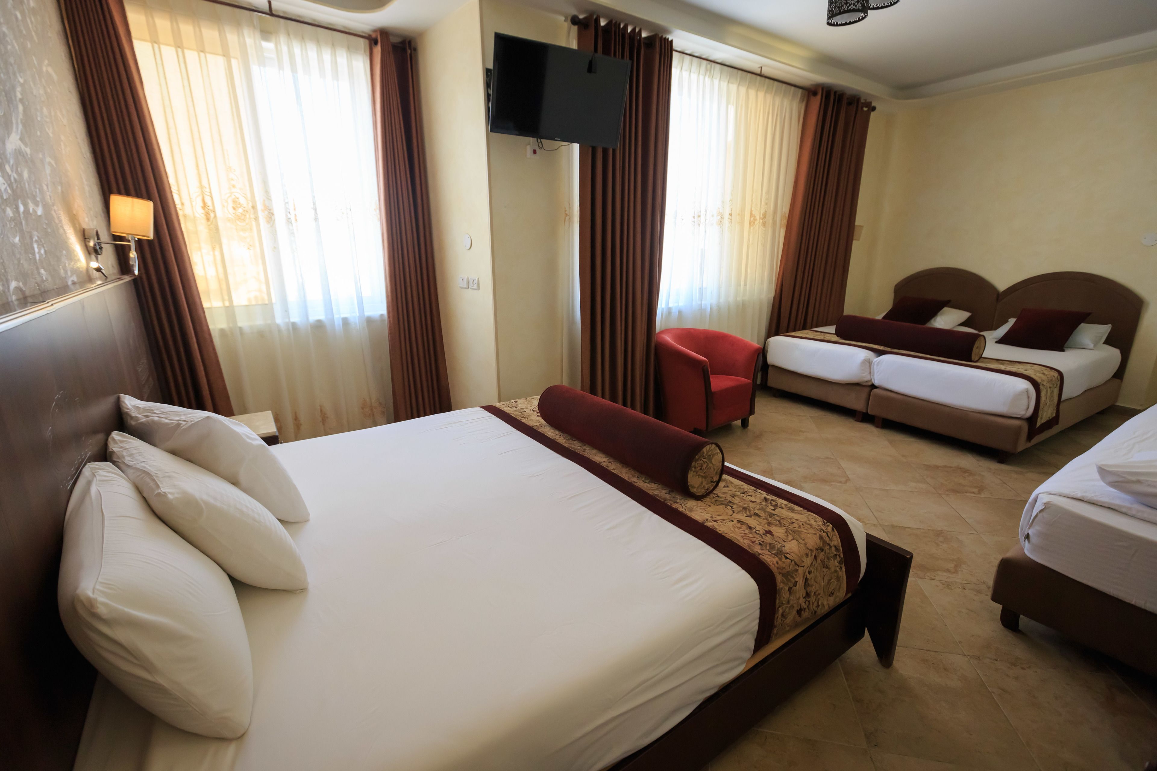 A hotel room with a large bed, a smaller bed, a TV mounted on the wall, and a red chair.