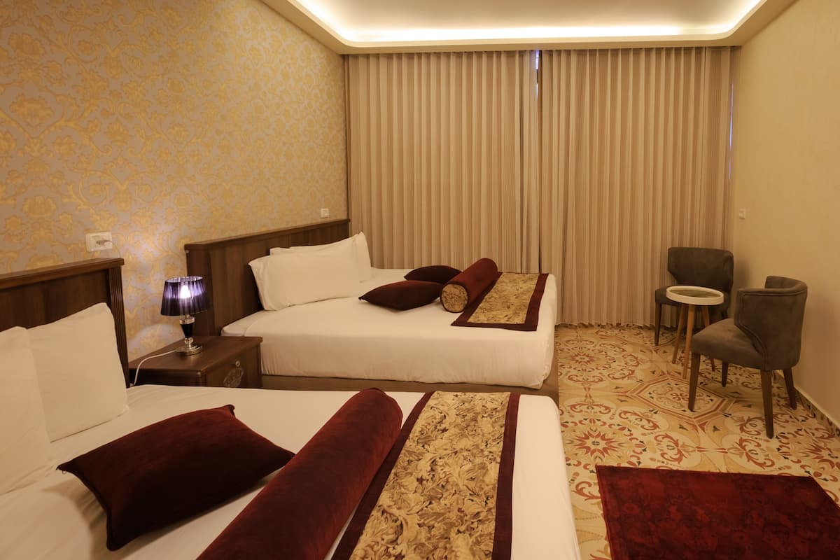 A hotel room with two beds, a nightstand with a lamp, a chair, and a small table.