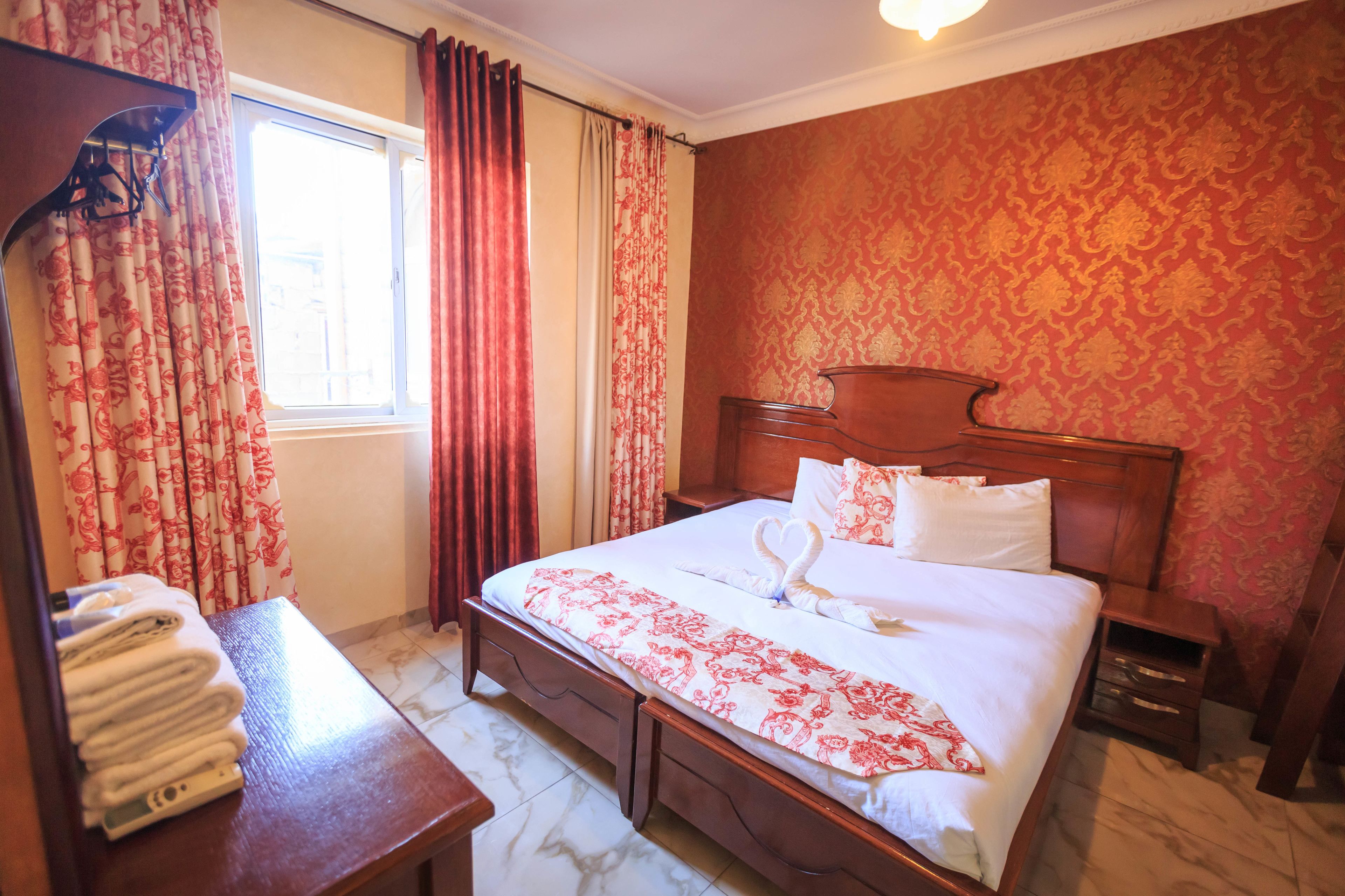 Een hotelkamer met een bed, nachtkastje, houten dressoir en een raam met gordijnen.