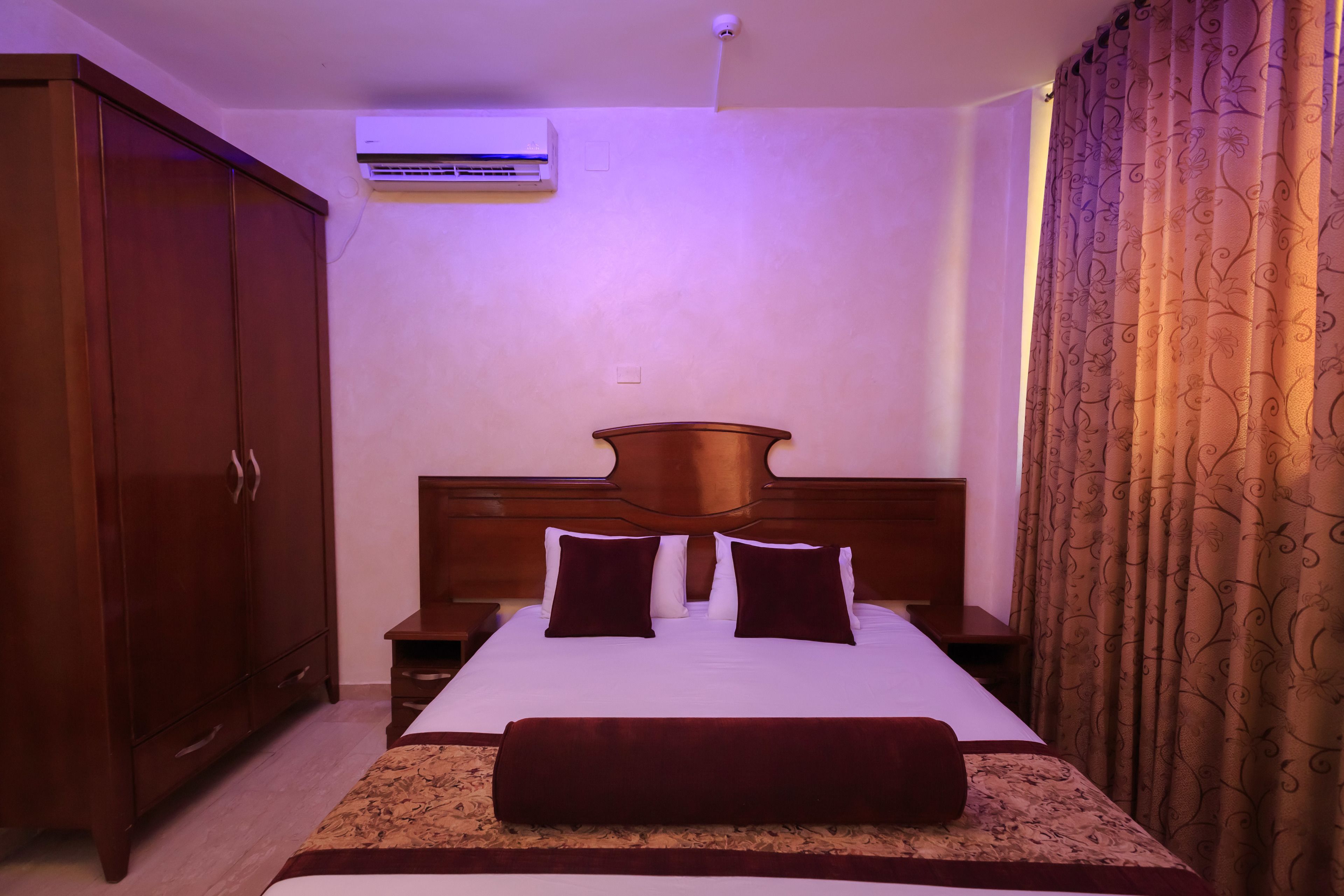 A hotel room with a wooden bed, a nightstand, a wardrobe, and a wall-mounted air conditioner.