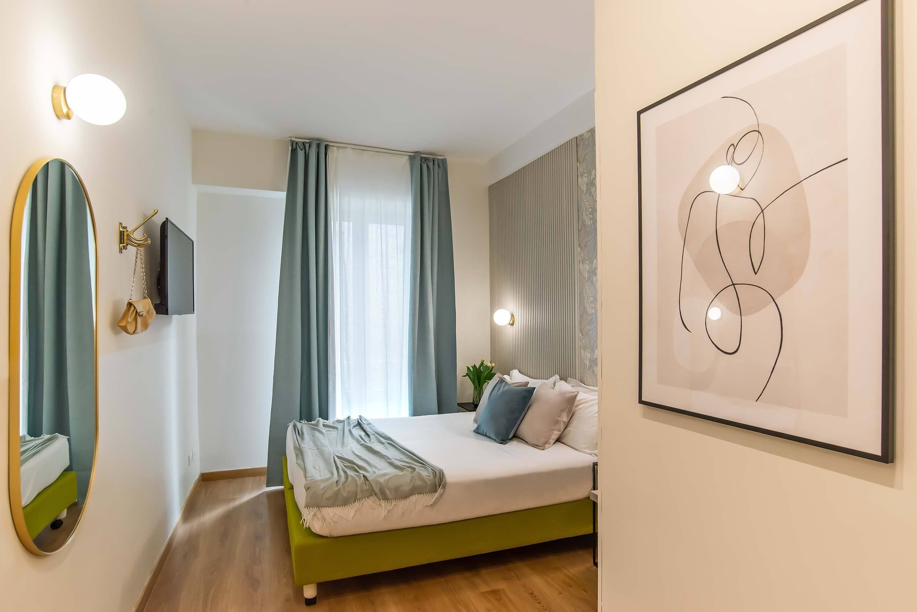 A modern bedroom with a green bed, a large mirror, a flat-screen TV, and a framed abstract painting.