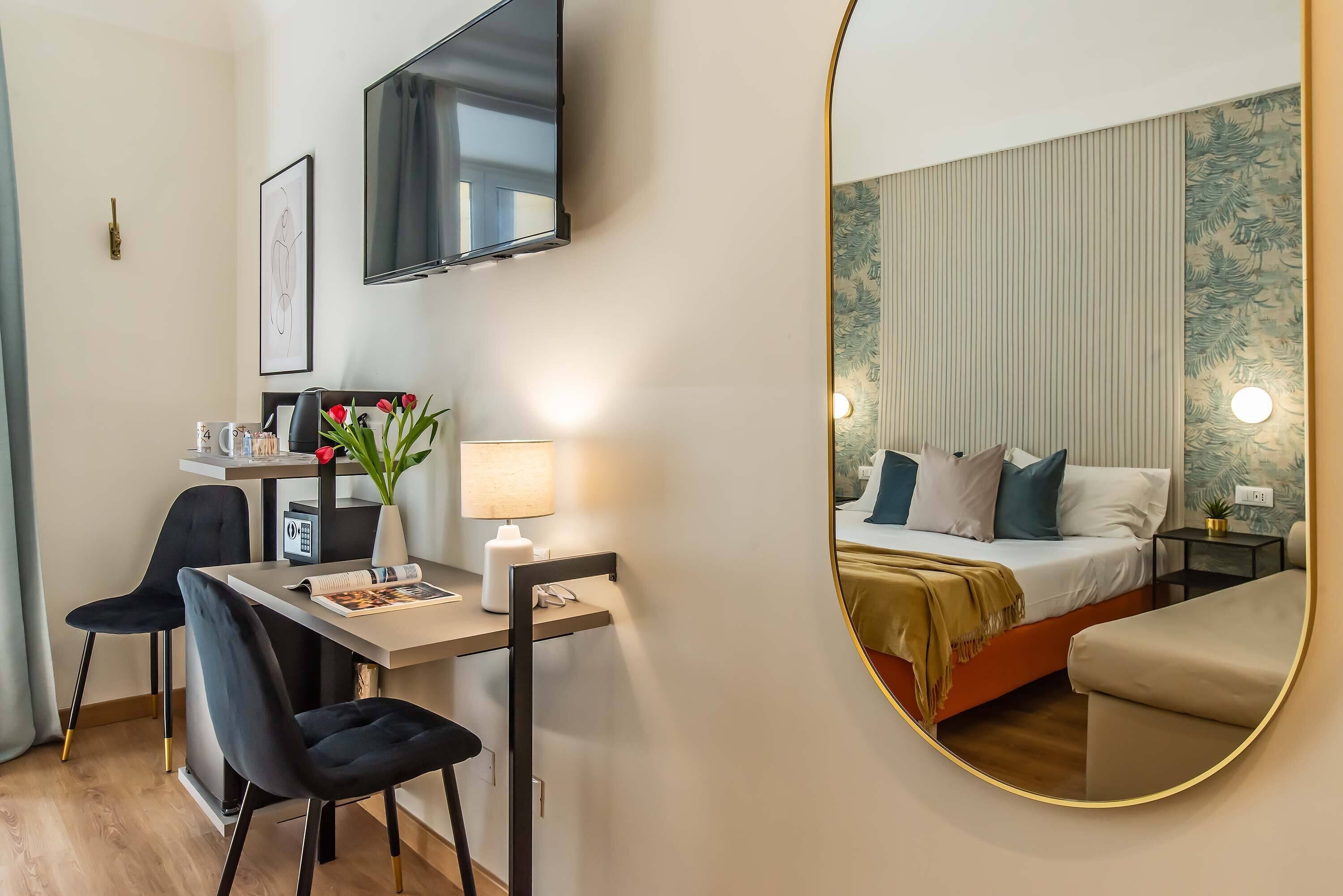 Ein modernes Hotelzimmer mit Bett, Nachttisch, Lampe und einem großen Spiegel.