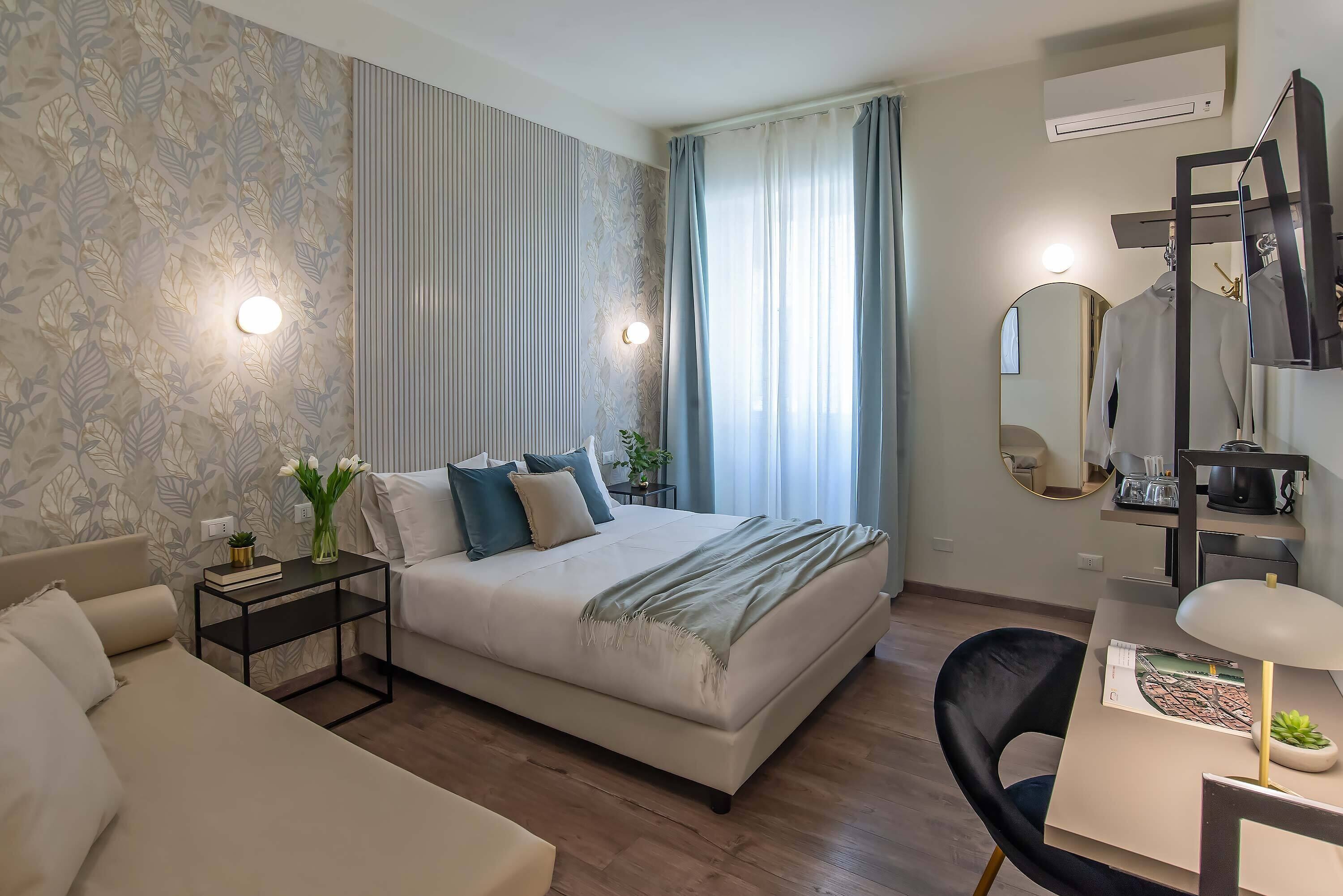 A modern bedroom with a large bed, a bedside table with a lamp, a chair, and a desk with a lamp.