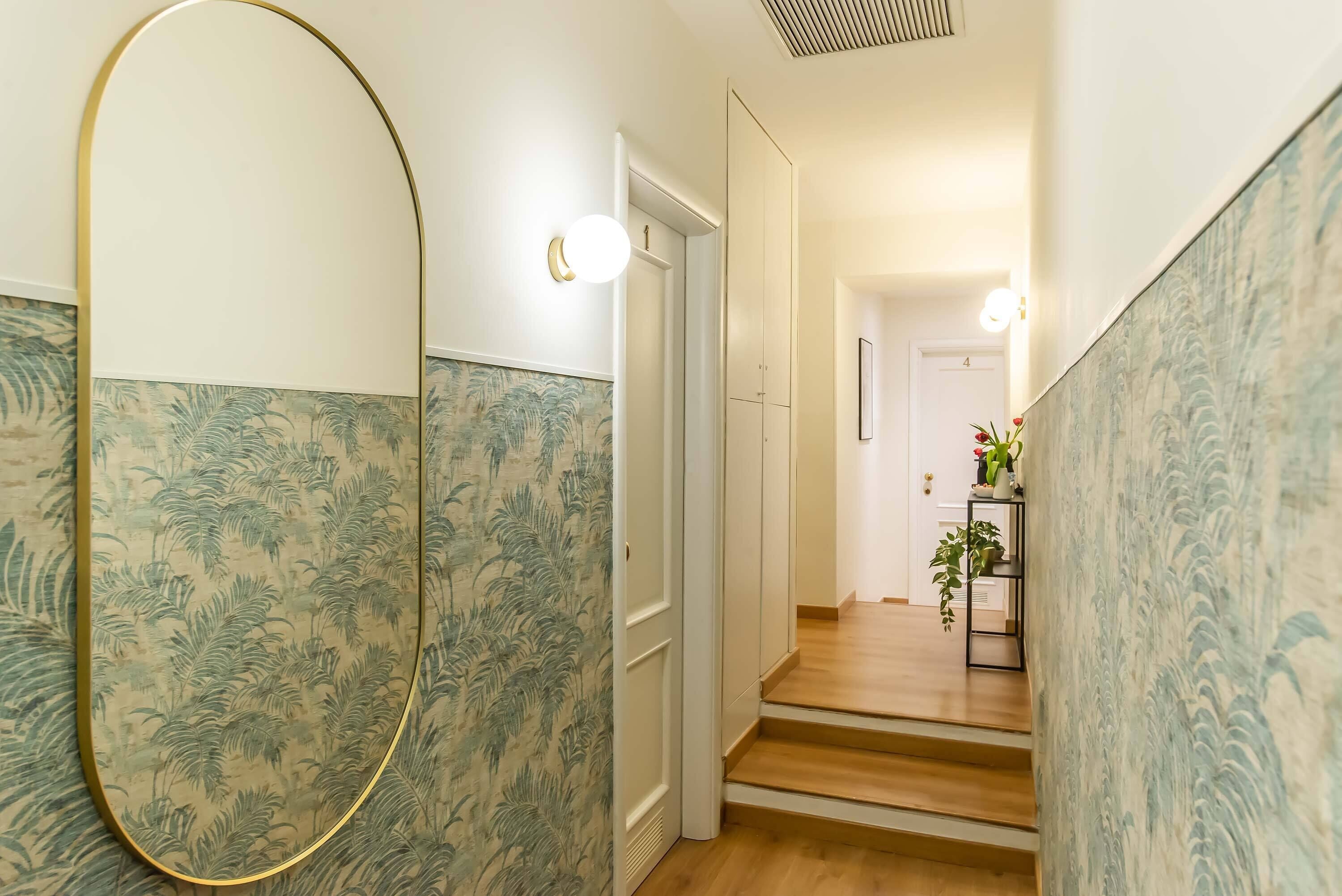 A hallway with patterned wallpaper, a large mirror, and a staircase leading to a room.