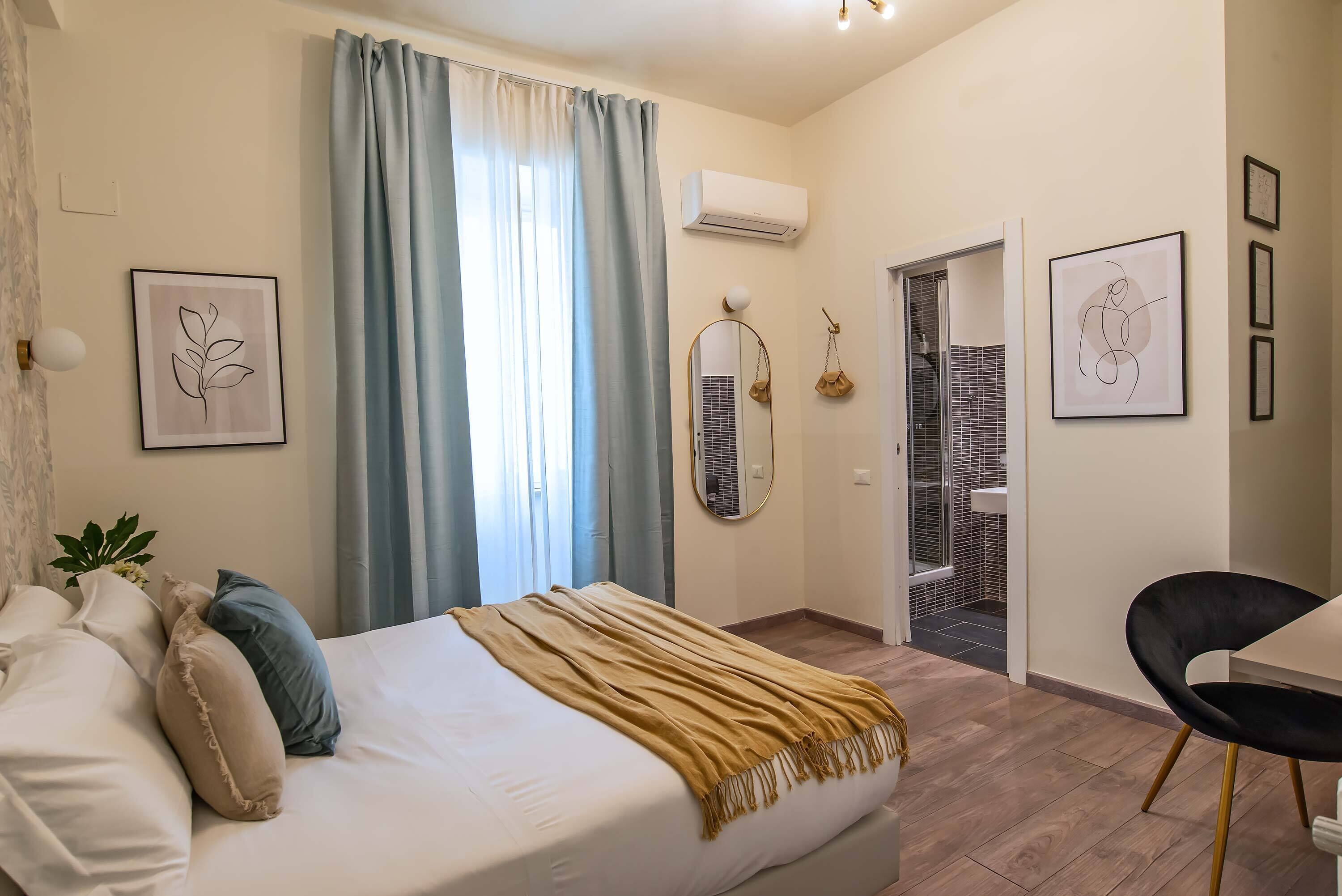 Une chambre à coucher avec un lit, une table de chevet, une chaise et une salle de bain visible à travers une porte ouverte.