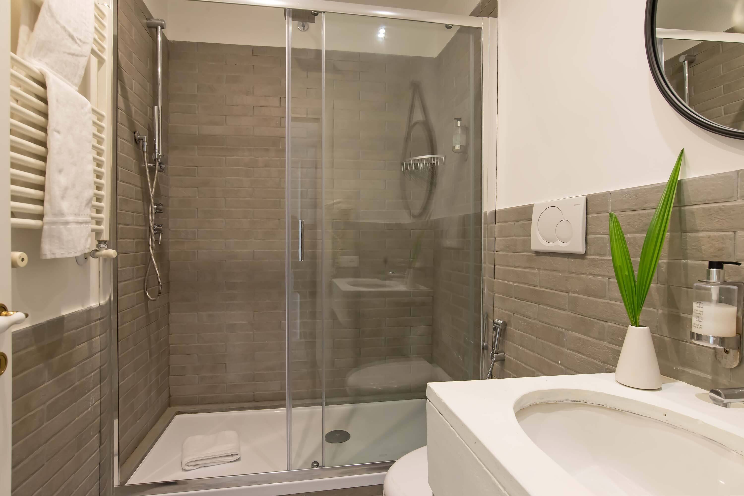 Un baño moderno con ducha de mampara de vidrio, un lavamanos blanco y un inodoro.
