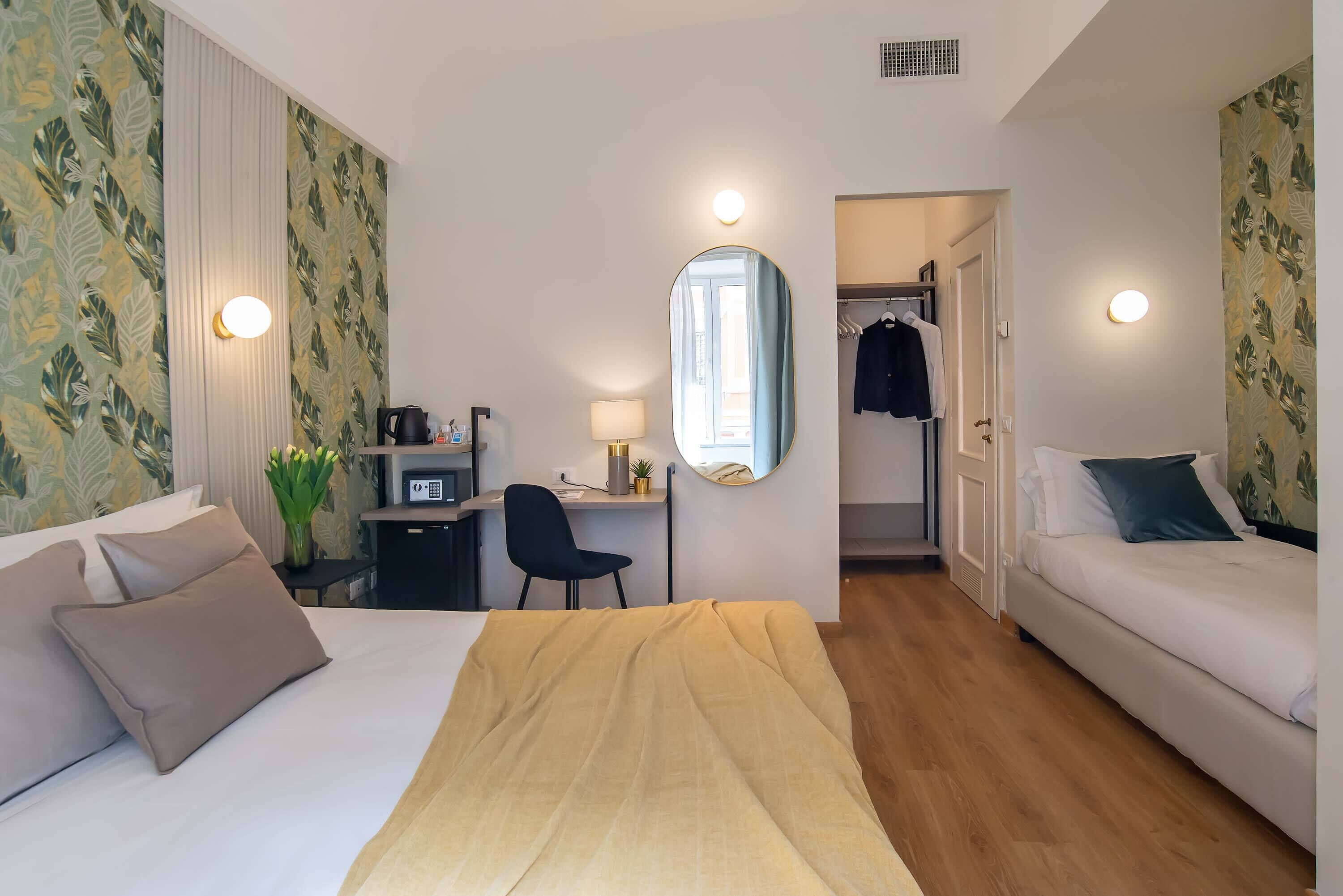 A hotel room with a bed, a desk, a chair, a mirror, and a wardrobe.