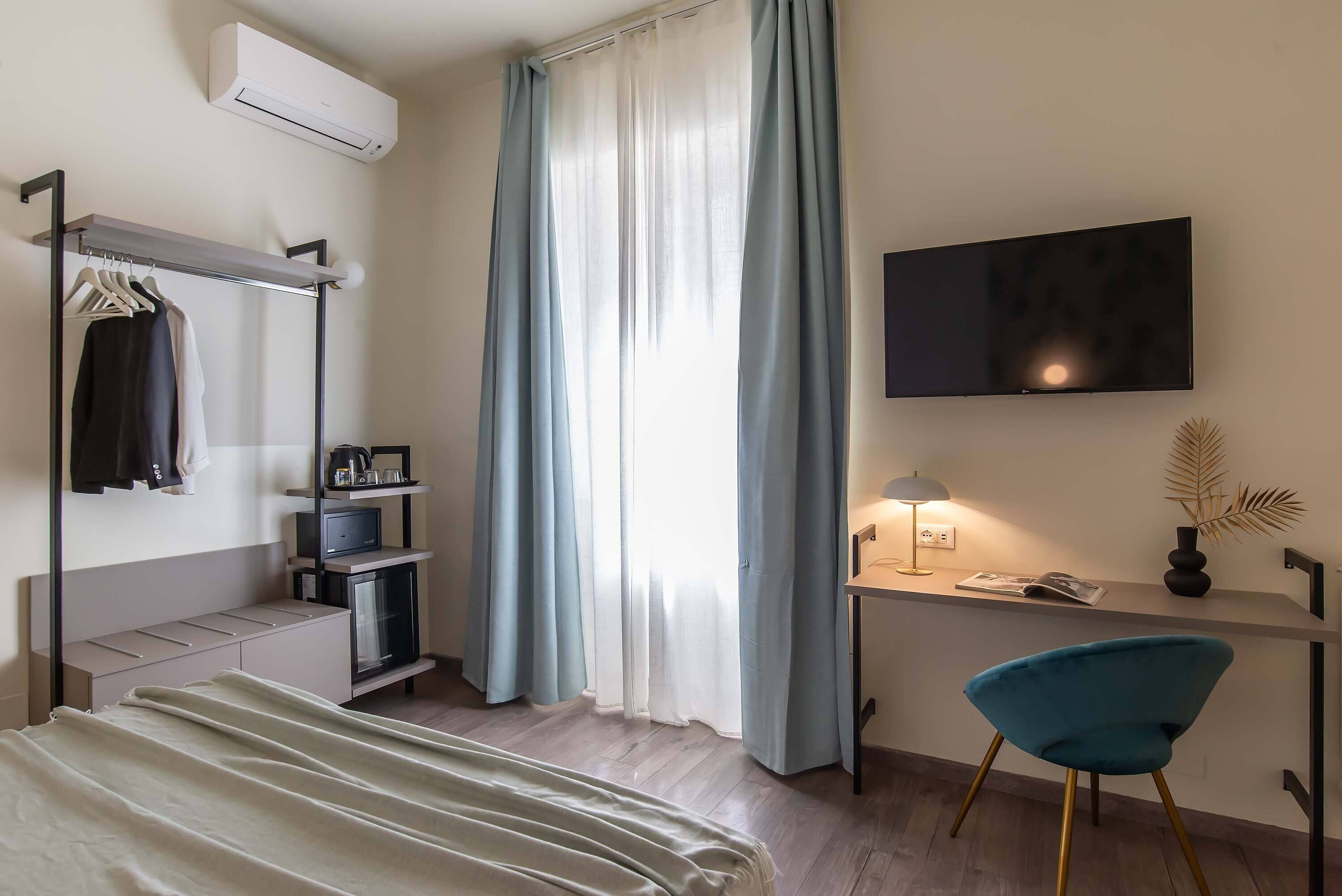 Habitación de hotel con cama, escritorio con lámpara, televisión, armario y una silla.
