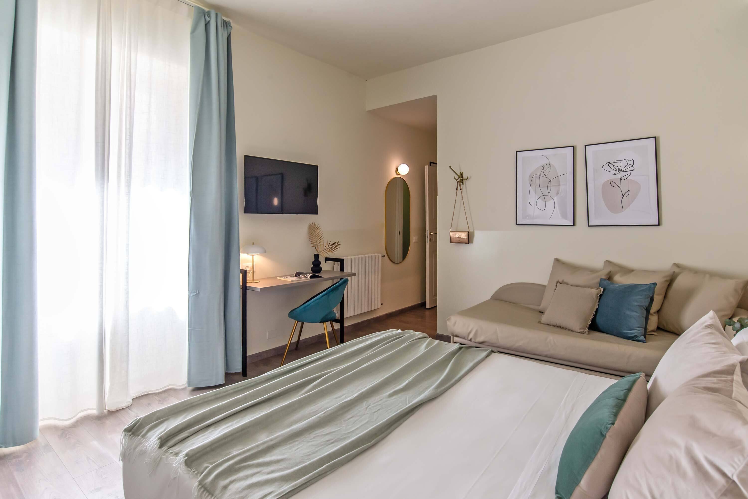 Ein Hotelzimmer mit Bett, Schreibtisch, Stuhl, Sofa und zwei Wandbildern.