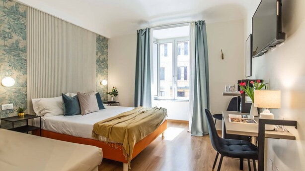 Een moderne hotelkamer met een bed, bureau, stoel, een televisie en een raam met gordijnen.